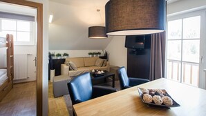 A modern living room with a wooden dining table, black chairs, a beige sofa, and a large hanging lamp.