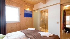 A wooden-paneled room with a bed, a glass shower enclosure, and a window with curtains.