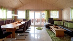 A modern interior with a wooden ceiling, a dining area with a long table and chairs, a sofa, and a small coffee table.