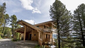 A wooden cabin with a covered porch and multiple balconies, surrounded by tall pine trees.