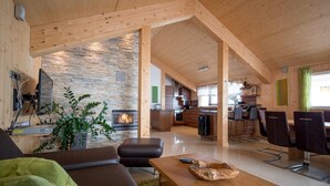 A modern living room with a fireplace, a dining area, and a kitchen in the background.