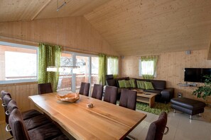 Ein modernes Wohnzimmer mit Holzboden, einem großen Esstisch, einer Couch und einem Fernseher.