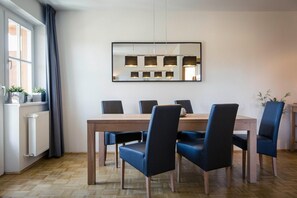 Uma área de refeições com mesa de madeira, seis cadeiras e luminárias pendentes.