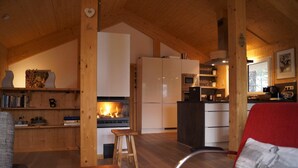 A cozy cabin interior with a fireplace, wooden beams, a kitchen area, and a red chair. - Modern cottage with whirlpool (Turracherhöhe)