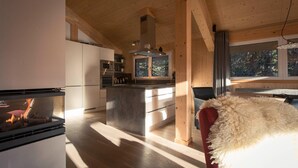 A modern kitchen with wooden beams, a central island, and a view of trees through a window. - Modern cottage with whirlpool (Turracherhöhe)