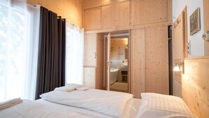 A hotel room with two beds, wooden walls, a bathroom visible through an open door, and a window with curtains. - Modern cottage with whirlpool (Turracherhöhe)