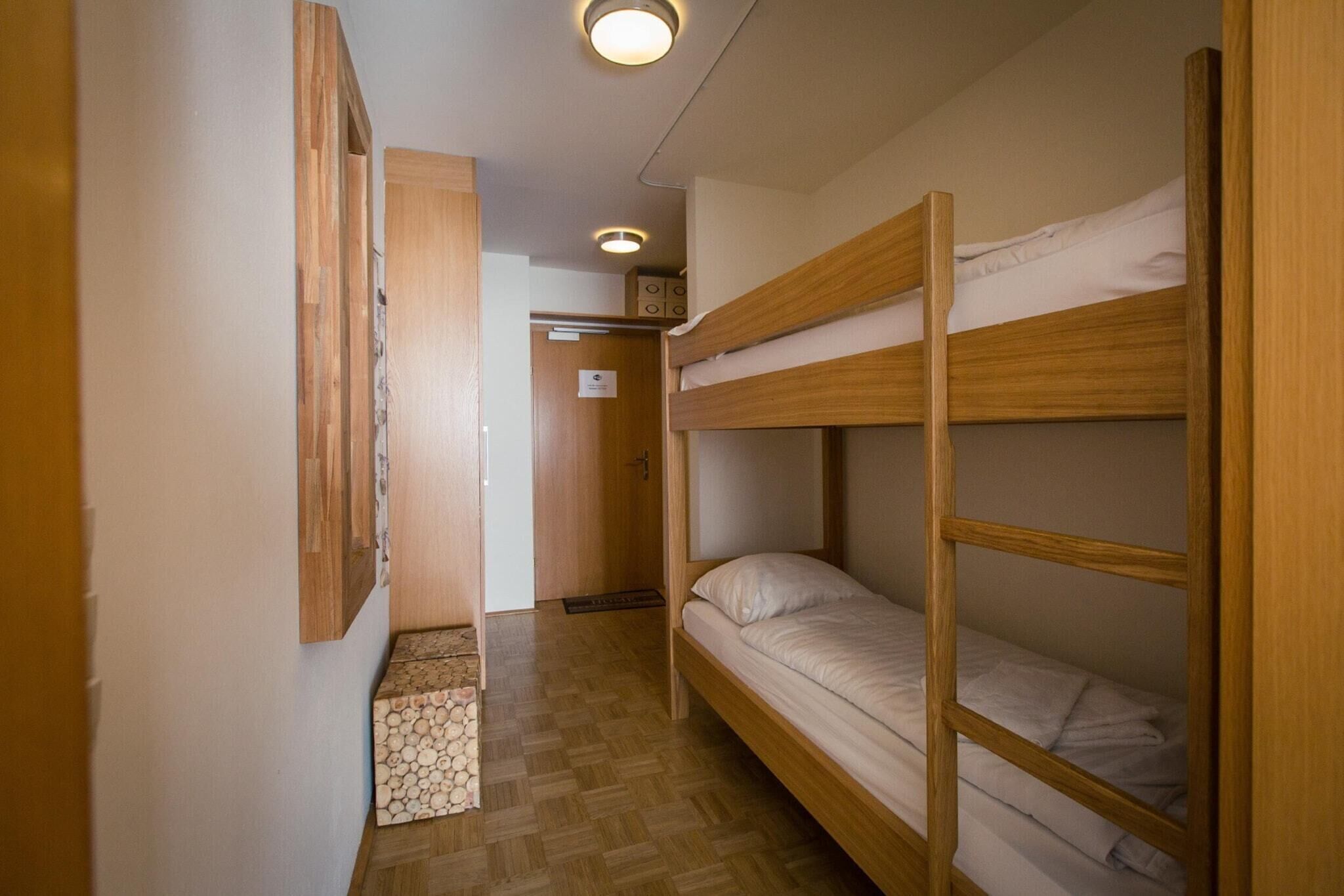Una camera con un letto a castello, pavimento in legno e un piccolo armadietto di legno.
