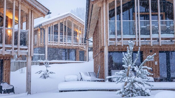 A wooden cabin with large windows and a covered outdoor seating area.