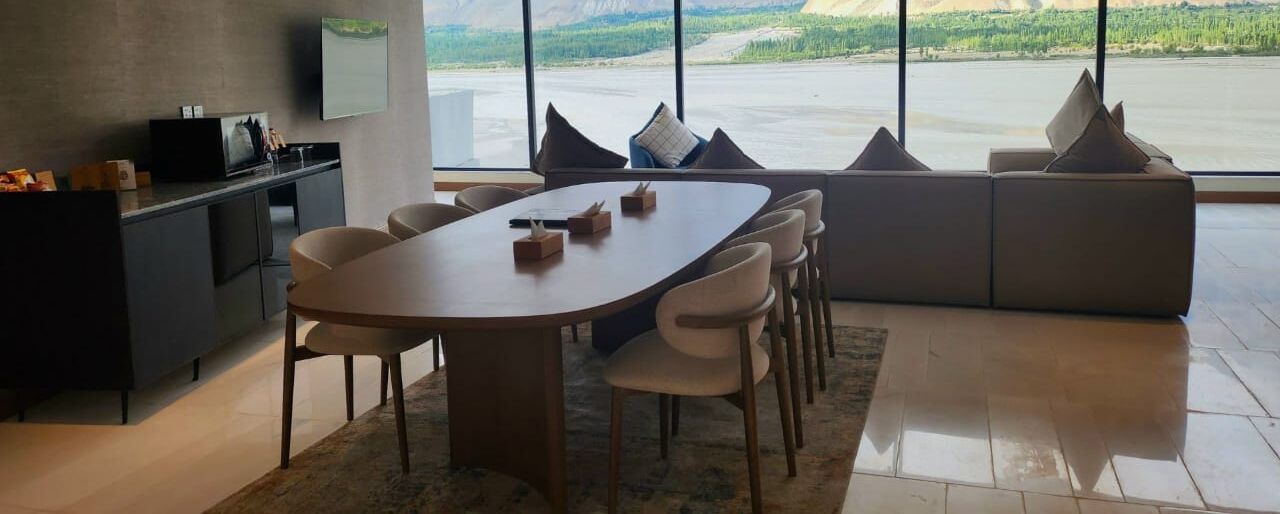 Ein moderner Essbereich mit einem großen, ovalen Tisch, mehreren Stühlen, einer Couch und Seeblick durch große Fenster.
