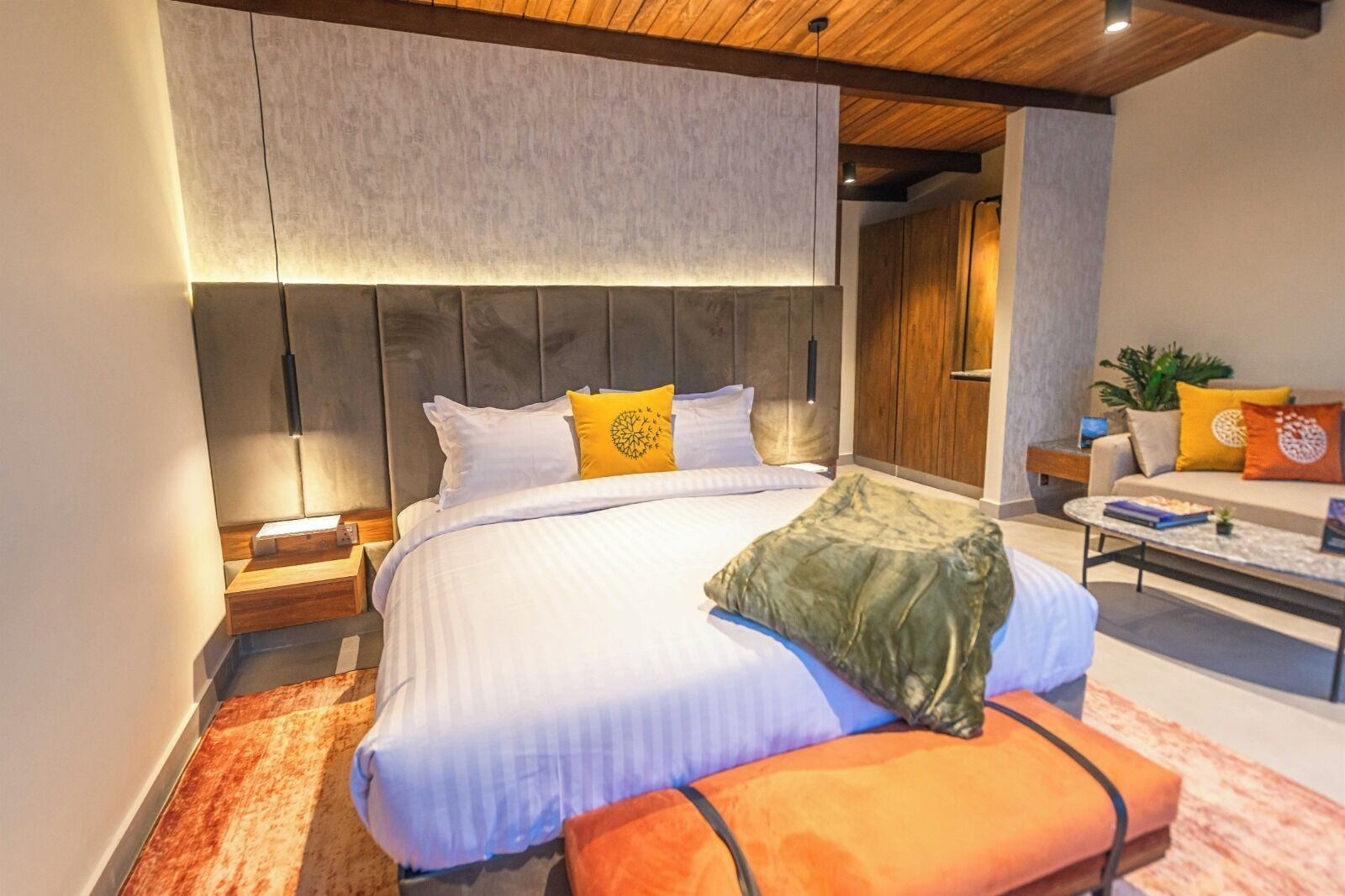 A modern bedroom with a large bed, a wooden ceiling, and a seating area with a sofa and coffee table.