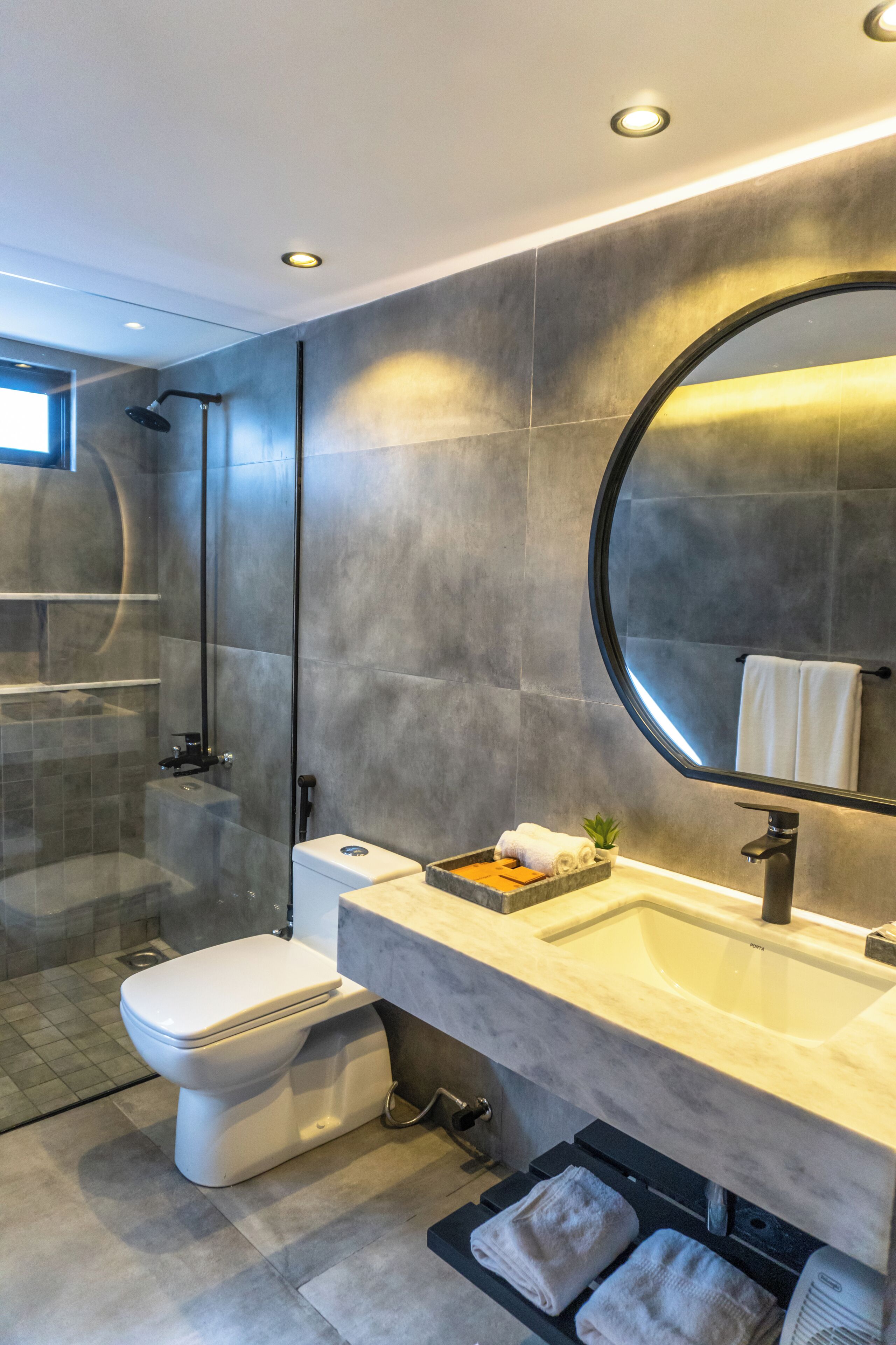 A modern bathroom with a glass-enclosed shower, a white toilet, a marble sink, and a large mirror.