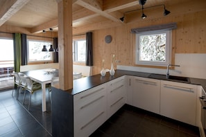 Eine moderne Küche mit weißen Schränken, einer schwarzen Arbeitsplatte und einem Fenster mit Blick auf schneebedeckte Bäume.