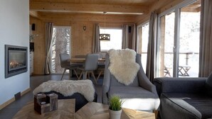 A cozy cabin interior with a fireplace, a dining area, and large windows offering a view of the outdoors. - Appealing chalet with infrared sauna (Turracherhöhe)
