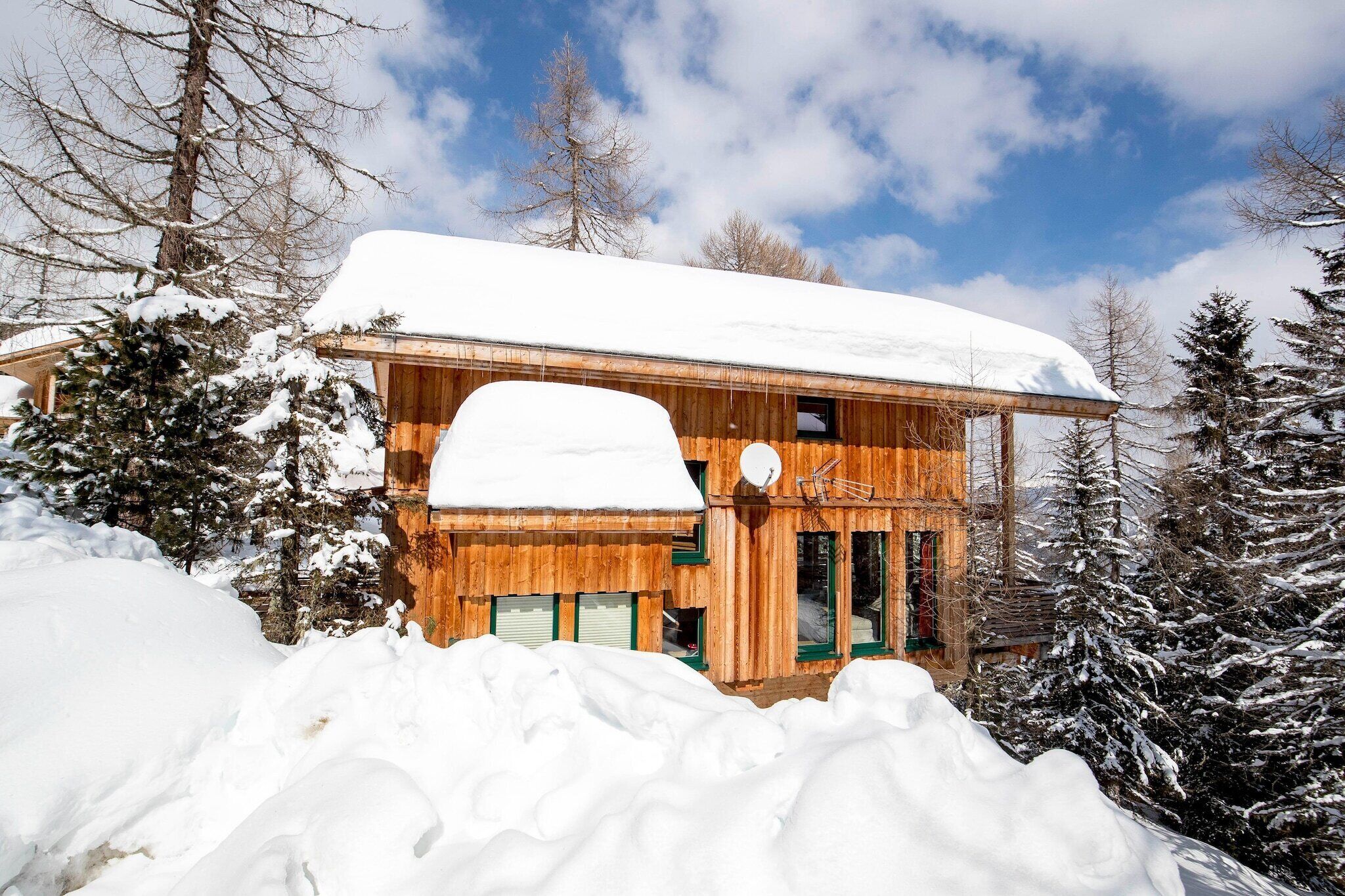 A wooden cabin with a snow-covered roof, surrounded by snow-laden trees and a clear sky.