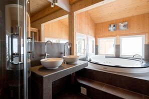 Un baño moderno con cabina de ducha de vidrio, dos lavamanos sobre encimera, una bañera independiente y paneles de madera.