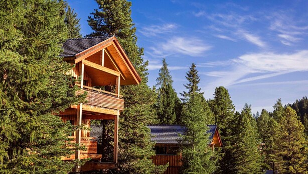Une cabane en bois dotée d’un balcon, entourée d’une forêt dense.