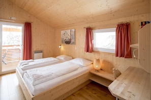 Ein Zimmer in einer Holzhütte mit zwei Betten, einem Vorhangfenster, einer Wandlampe und einem kleinen Tisch.