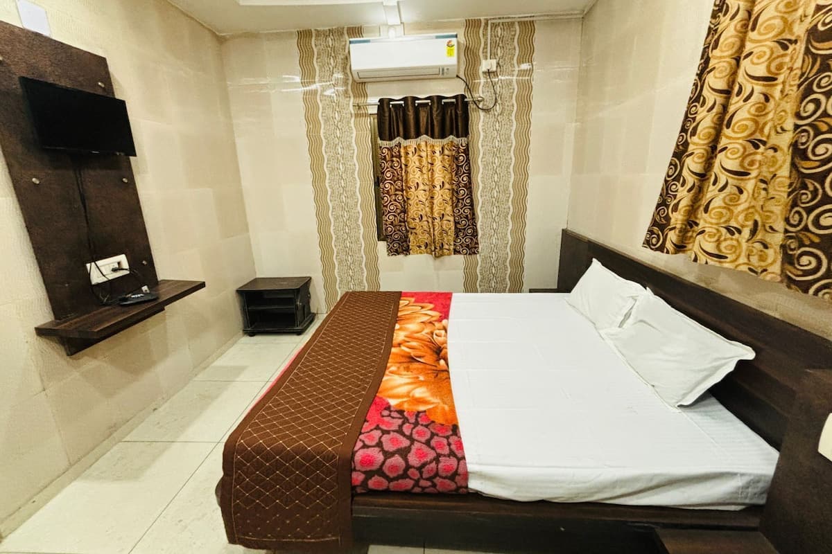 Quarto de hotel com cama, uma mesinha, TV na parede e janela com cortinas estampadas.