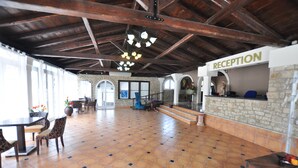 Ampla área de recepção com piso de azulejos, balcão de atendimento e escada para os andares superiores.
