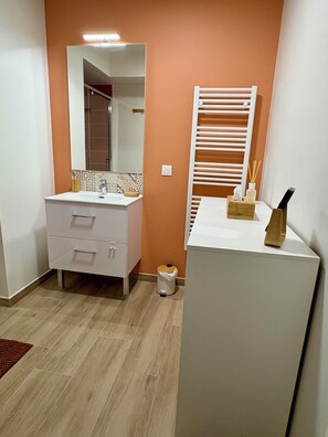 A bathroom with a white sink, mirror, and towel rack. There is a trash can and a small wooden box with a knife on the counter.