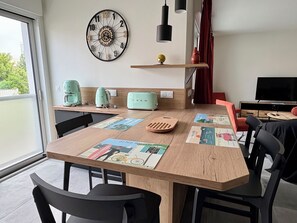 A modern kitchen with a wooden table, black chairs, a clock, and a TV.