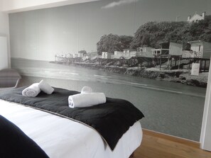 Ein Hotelzimmer mit einem großen Bett, Blick auf eine Küstenlandschaft und zwei zusammengerollte Handtücher auf dem Bett.