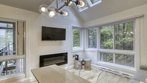 A modern kitchen with a large island, a flat-screen TV, and large windows offering a view of the outdoors.