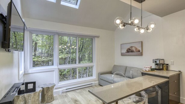 A modern kitchen with a large window, a grey sofa, and a dining area with a glass table.