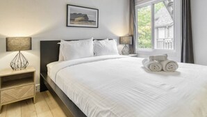 A neatly made bed with white linens, a headboard, and a bedside table with a lamp.