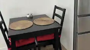 Une table à manger avec deux chaises, un réfrigérateur et deux tableaux encadrés accrochés au mur.