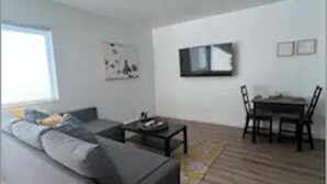 Un salon moderne avec un canapé gris, une petite table basse et un coin repas comprenant une table et des chaises.