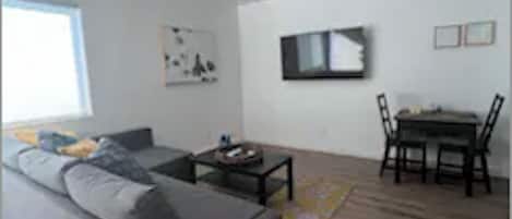 A modern living room with a grey sofa, a small coffee table, and a dining area with a table and chairs.