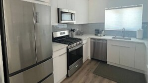 Une cuisine moderne dotée d’appareils électroménagers en acier inoxydable, de meubles blancs et d’un plancher en bois.