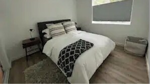 Une chambre à coucher avec un lit, une table de chevet, une fenêtre et une poubelle.