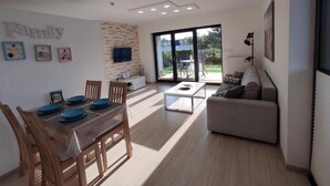 Un salon moderne comprenant un coin repas, un canapé et un téléviseur fixé au mur.