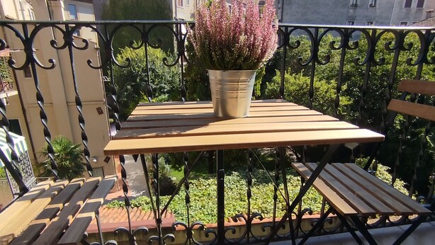 A balcony with a table and chairs, a potted plant, and a view of surrounding buildings.