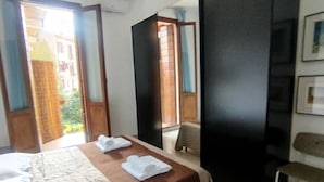 A hotel room with a bed, a desk, and a chair. There is a window with a view of buildings outside.