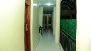 A corridor with a wooden door, a metal railing, and a green fence.