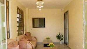 A spacious living room with a beige sofa set, a coffee table with a vase of flowers, and a large window with a view.