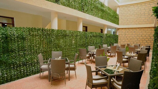 A covered outdoor dining area with wicker furniture and a green wall.