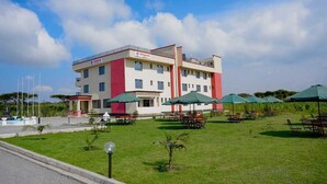 A hotel with a red and white facade, outdoor seating area with umbrellas, and a well-maintained lawn.