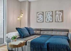 Una sala de estar moderna con un sofá gris, almohadas azules, una manta azul, una lámpara de pie y arte abstracto en la pared.