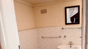 A small bathroom with a white sink, a mirror, and patterned tiles on the walls and floor. - Lotus House Harare (Harare)