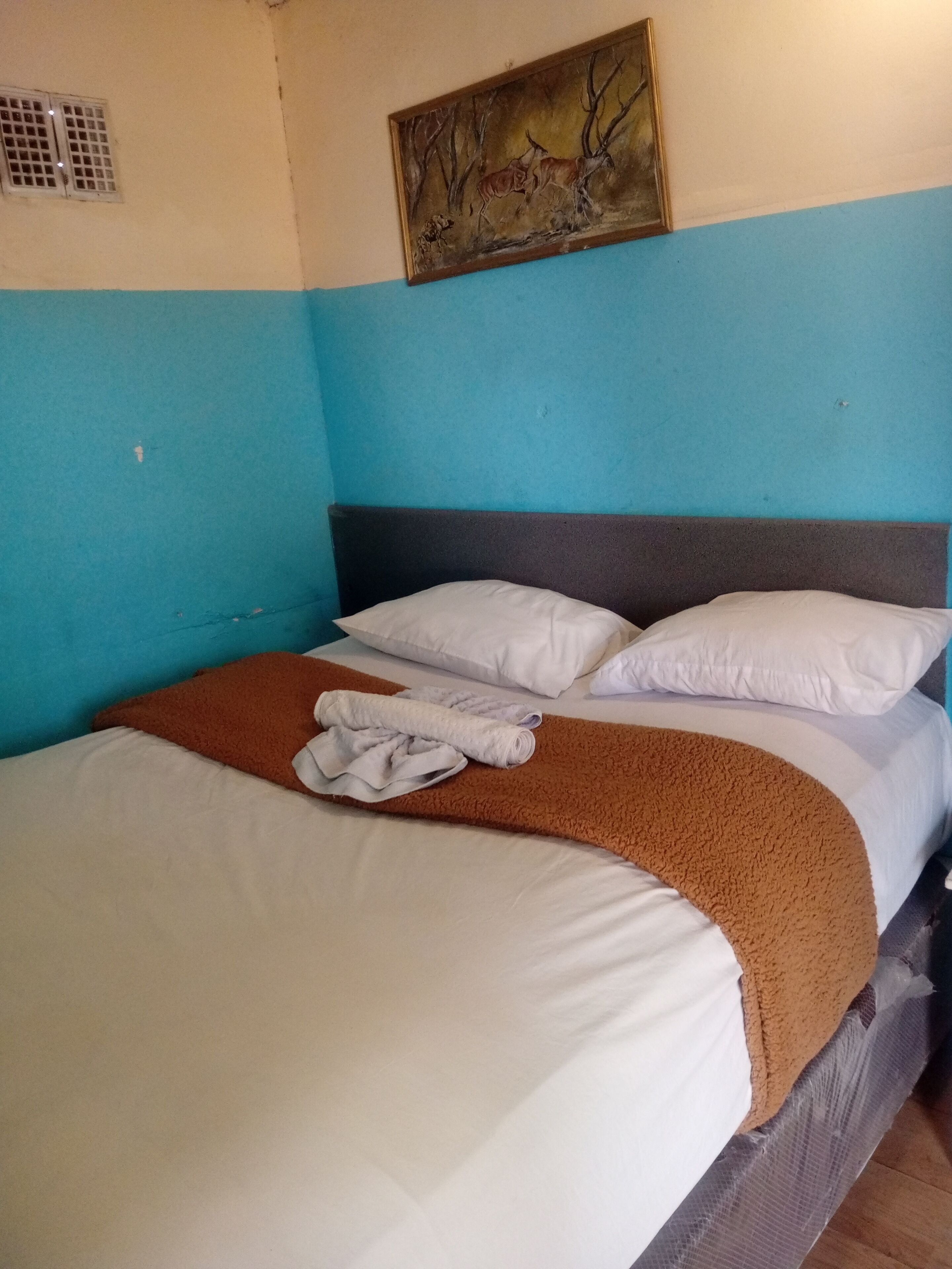 A bed with white and brown linens, a brown throw blanket, and a painting above it.