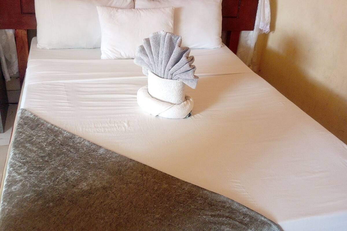 A neatly made bed with white linens, a grey throw blanket, and a decorative shell-shaped towel.