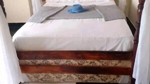 A four-poster canopy bed with white linens and a blue hat on the pillow. - Lotus House Harare (Harare)