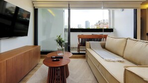 A modern living room with a sofa, a coffee table, a TV mounted on the wall, and a sliding glass door leading to an outdoor balcony.