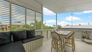 A covered outdoor seating area with a table and chairs, a cushioned bench, and potted plants.
