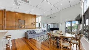 A modern living space with a wooden floor, a gray sofa, a dining table with chairs, and a TV mounted on the wall.