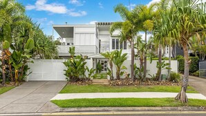 A modern two-story house with a white exterior, a covered front porch, and a well-maintained garden with tropical plants.